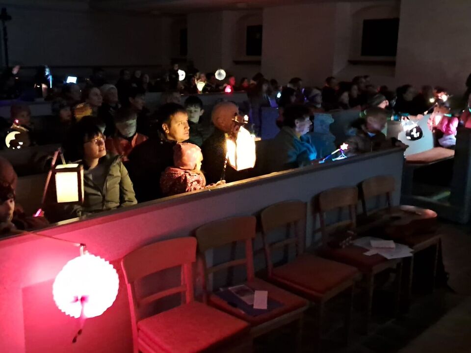 in der dunklen Kirche sitzen die Besucher mit leuchtenden Laternen und singen ein Lied.