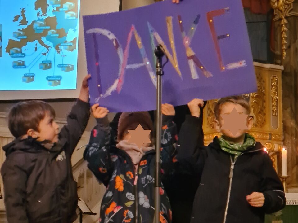 Drei Kinder halten ein selbst gemalten Bild mit dem Wort Danke.