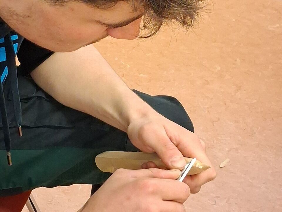 Ein Junge schnitzt mit dem Messer eine Baumspitze.