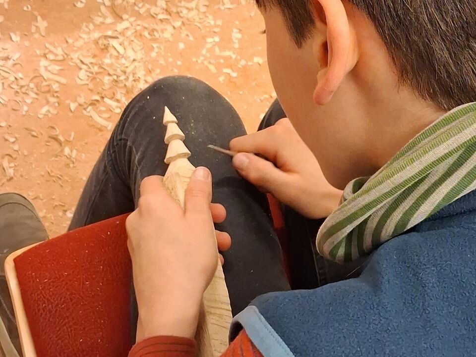 Ein Junge schnitzt mit dem Messer eine Baumspitze.