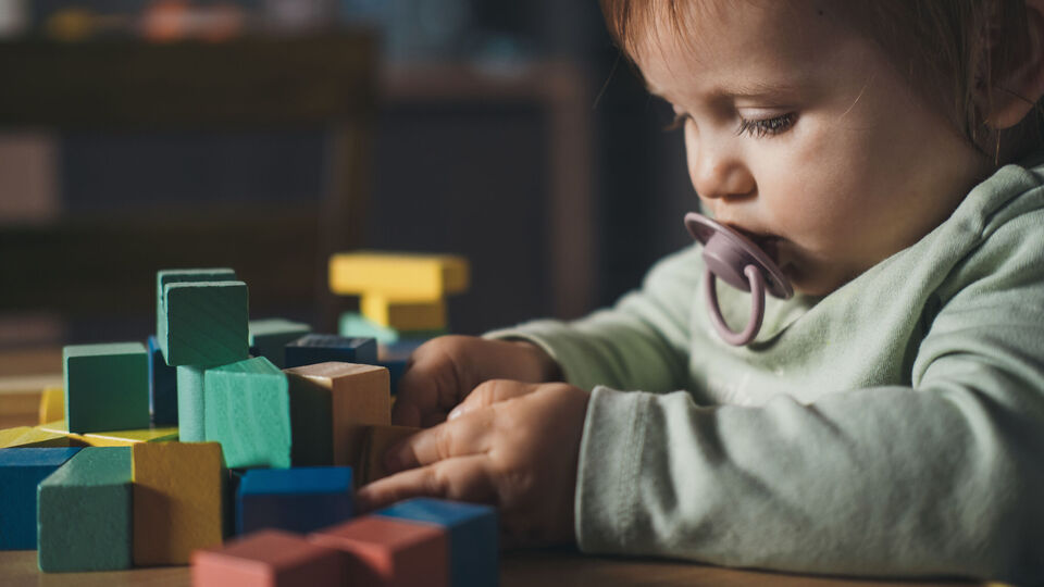 Baby girl playing with colorful toy blocks sitting at table. Building tower of block toys. Children education.