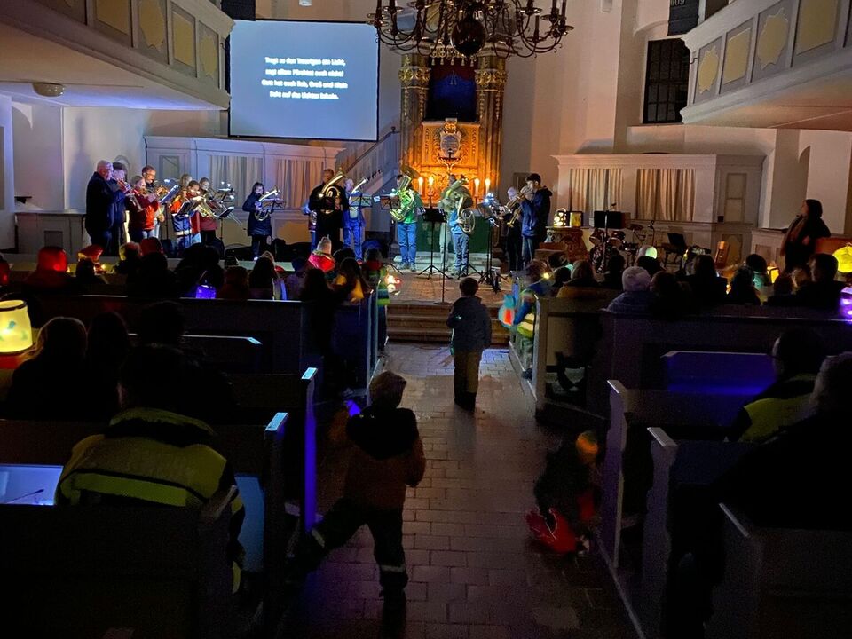 Ein Blick von den hintersten Kirchenbänken nach vorn. Man sieht die Menschen in den Kirchenbänken sitzen.