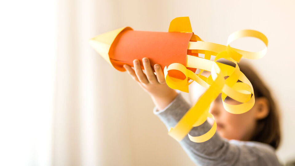 A portrait of a cute little girl playing with a hand made card stock rocket.Children creativity concept. Kids art themed photo.Preschooler craft.