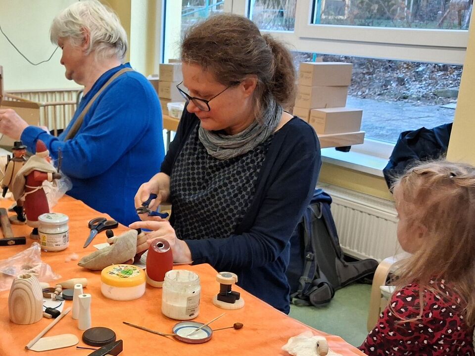 Eine Frau setzt aus vielen Einzelteilen einen Räuchermann zusammen. Es ist zu erkennen, dass es ein roter Weihnachtsmann wird.
