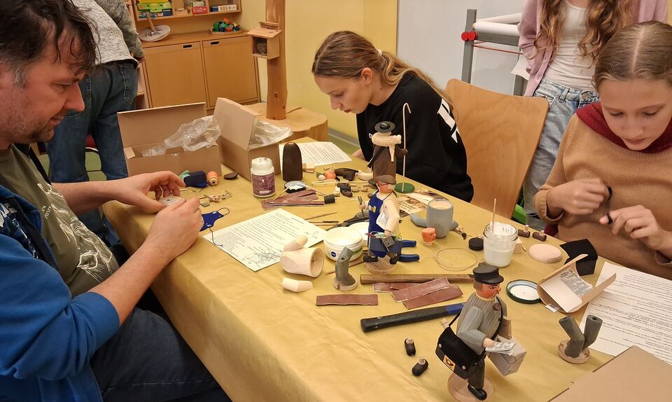 Drei Personen setzen aus Einzelteilen einen Räuchermann zusammen.