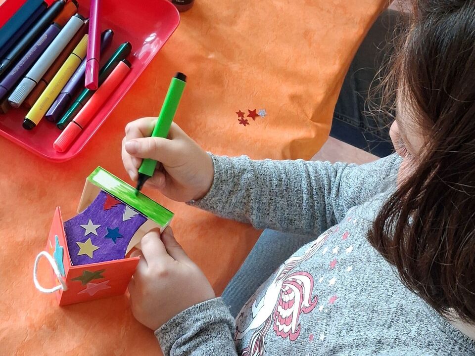 Ein Mädchen bemalt ein kleines Vogelfutterhäuschen.